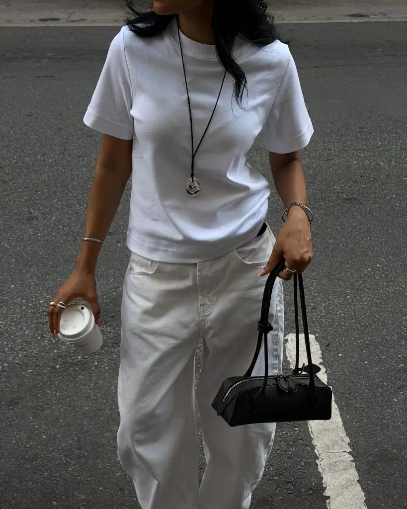 All-white outfit with white t-shirt, white wide-leg jeans, pendant necklace and small black bag