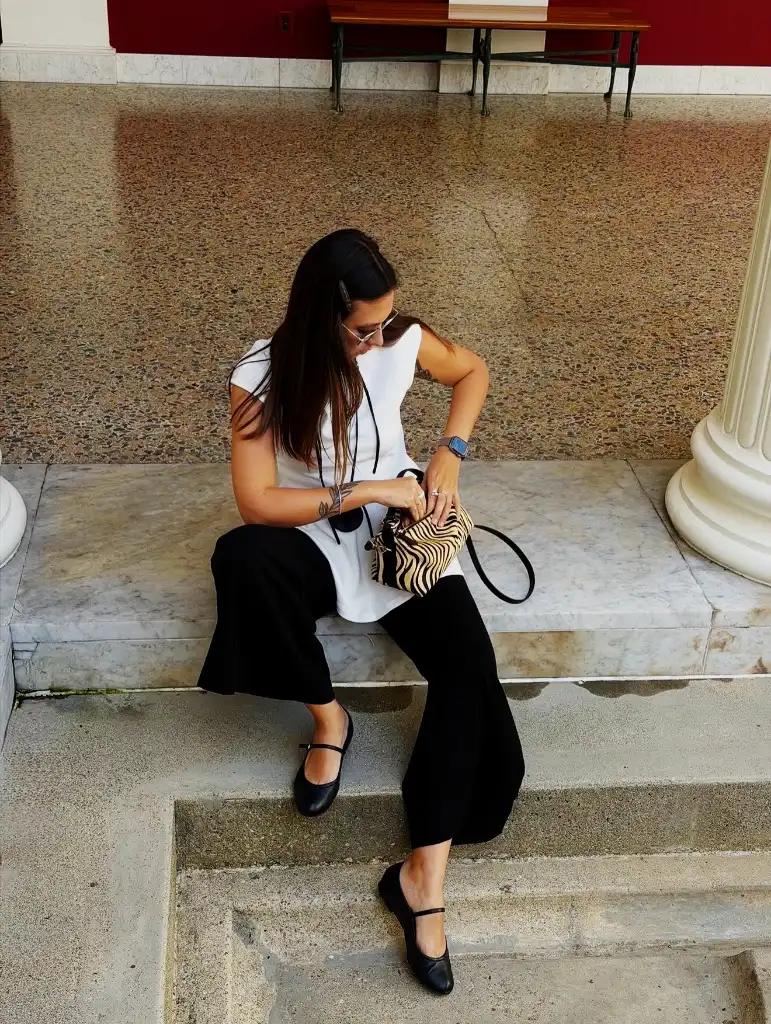 White sleeveless top with black wide-leg trousers, mary jane flats, and zebra bag