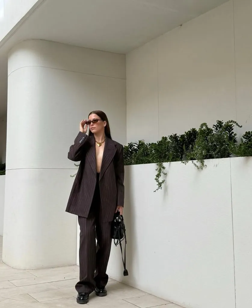 Dark brown pinstripe oversized suit with gold necklace and black bag