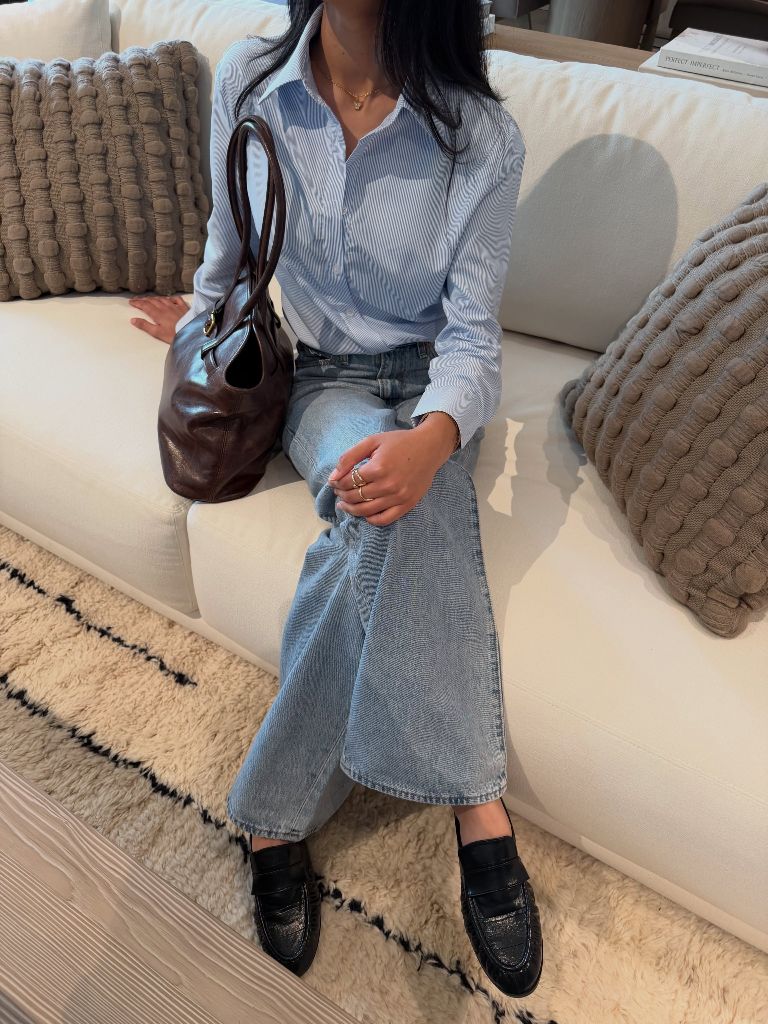 Blue striped button-up shirt with light wash jeans, black loafers, and burgundy leather bag