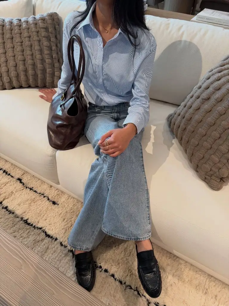 Blue striped button-up shirt with light wash jeans, black loafers, and burgundy leather bag