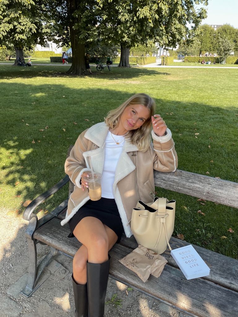 Shearling aviator jacket with black mini skirt and tall boots on a park bench