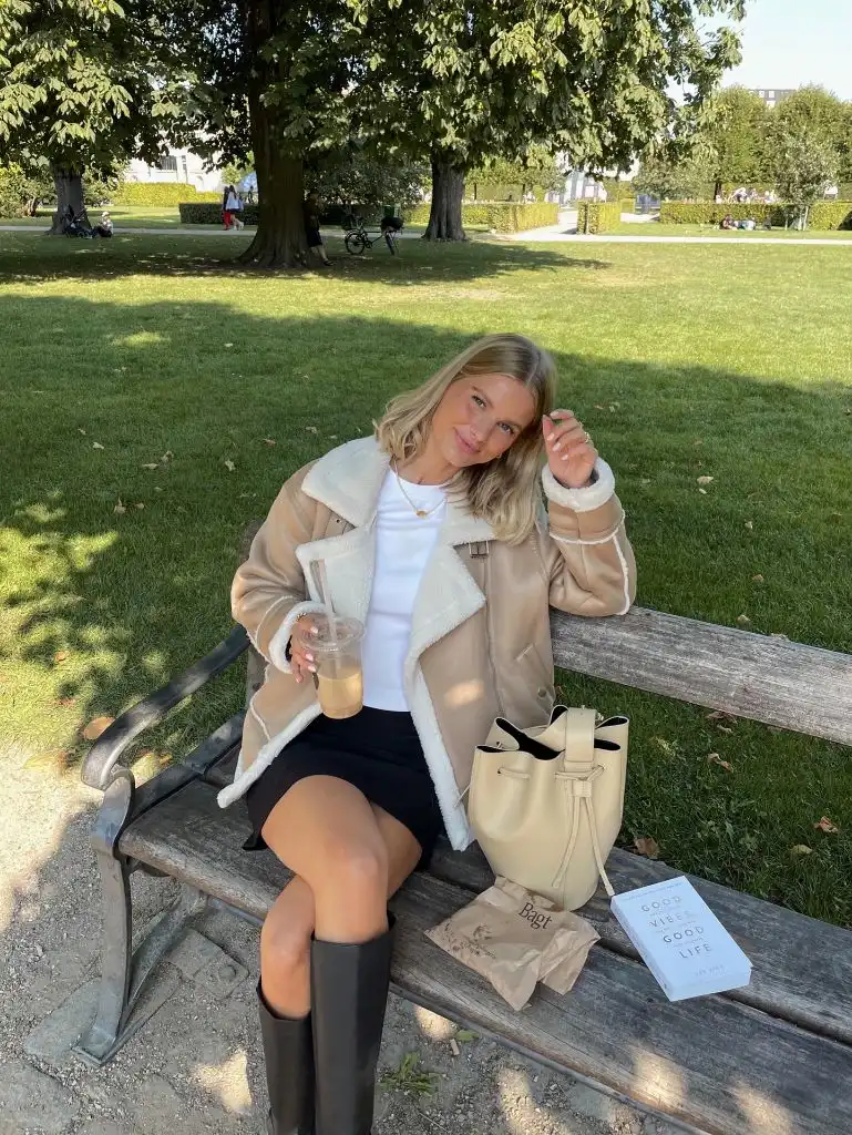 Shearling aviator jacket with black mini skirt and tall boots on a park bench