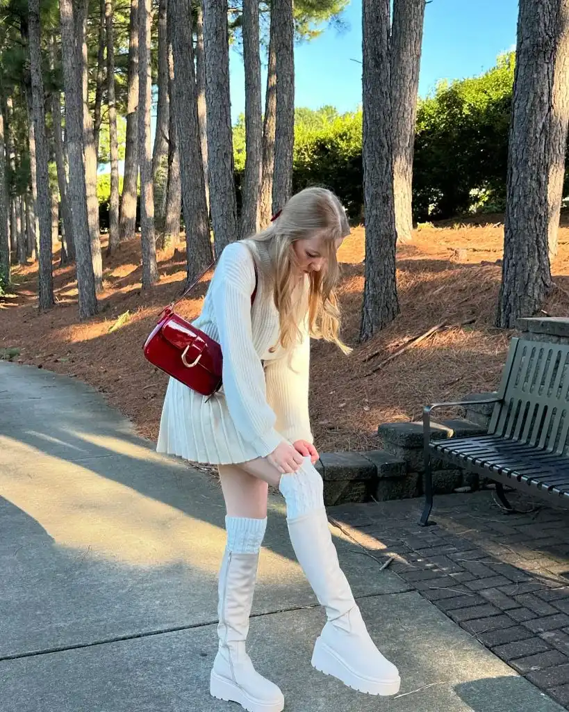 All-white outfit with cream sweater, pleated mini skirt, white platform boots, cable-knit leg warmers, and red patent bag