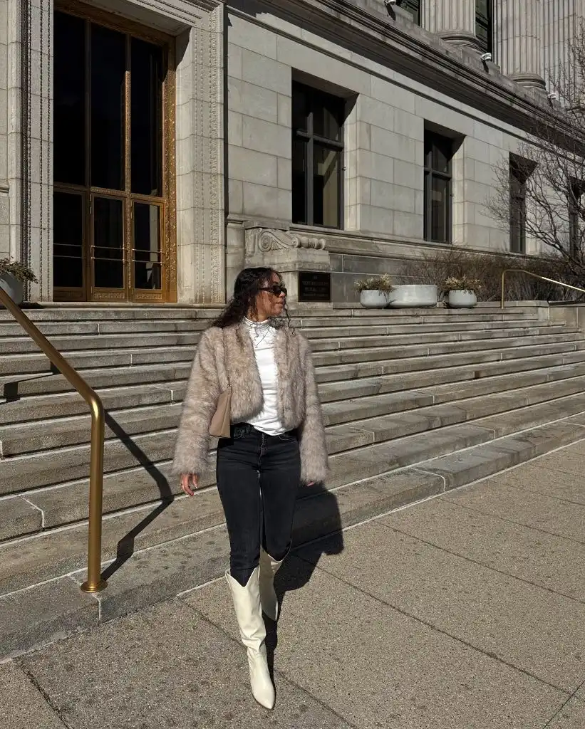 Woman in blush faux fur jacket with white boots on city steps