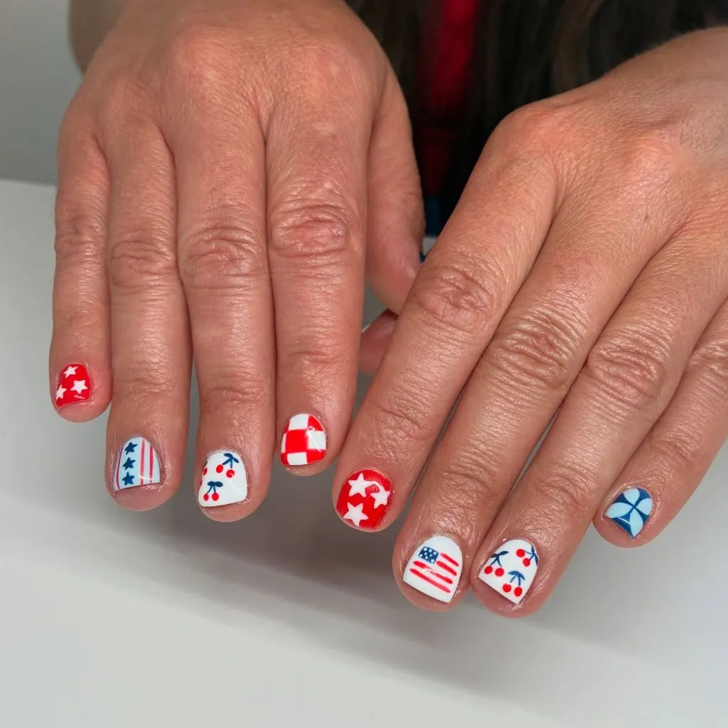 Red white and blue patriotic nail art with stars stripes cherries on short nails August nails color 2026 ideas