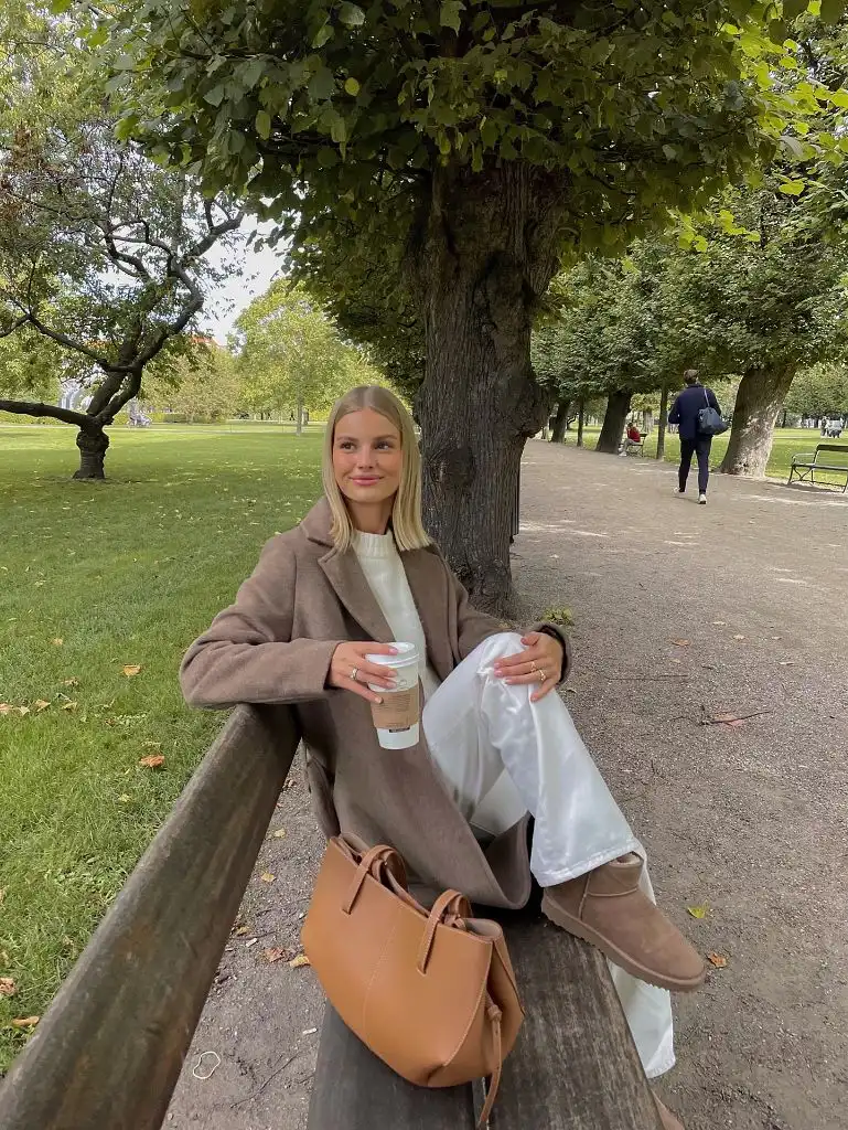 Taupe oversized coat with white trousers and brown UGGs in a park