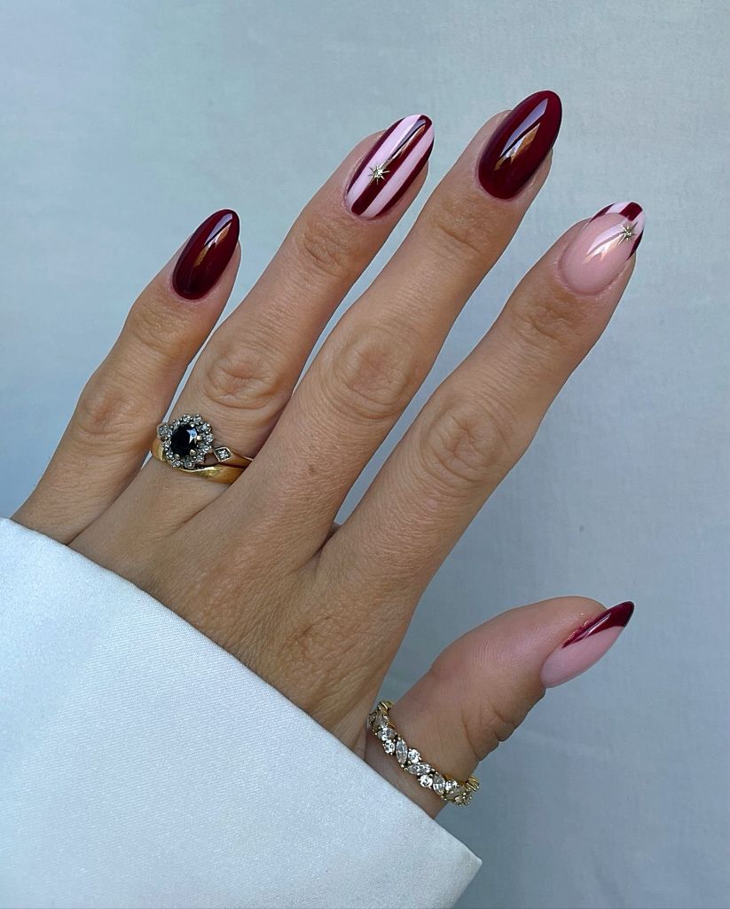 Deep wine almond nails with gold star accents, elegant August nail design 2026