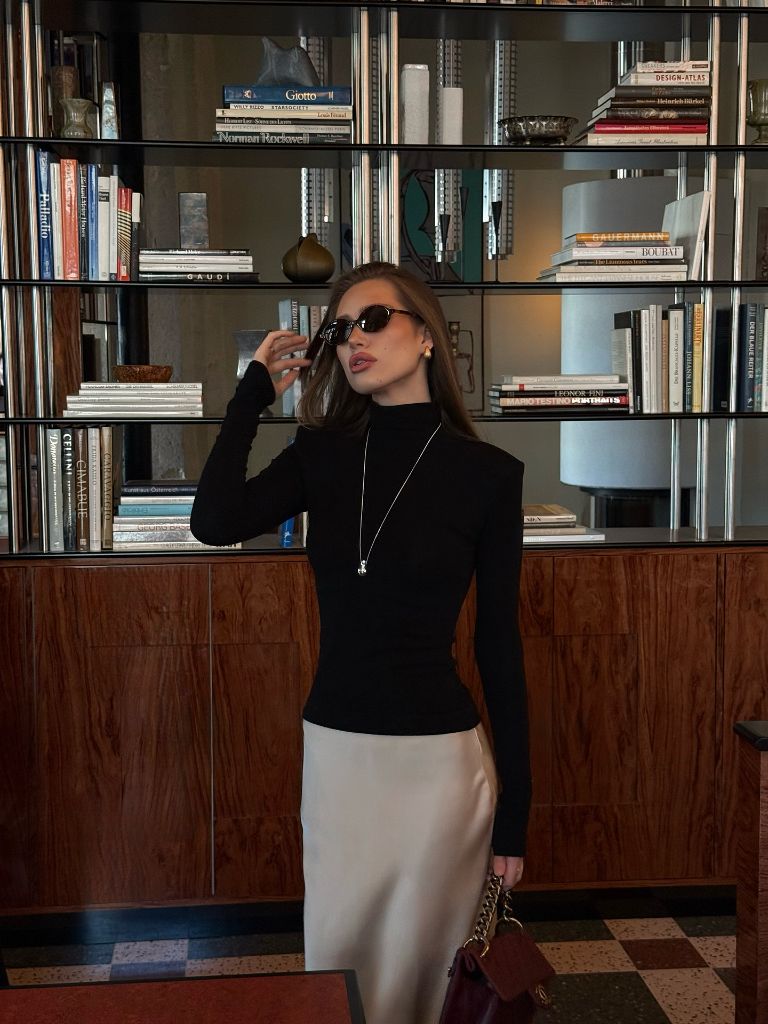 Front-facing black turtleneck and champagne satin skirt in hotel library