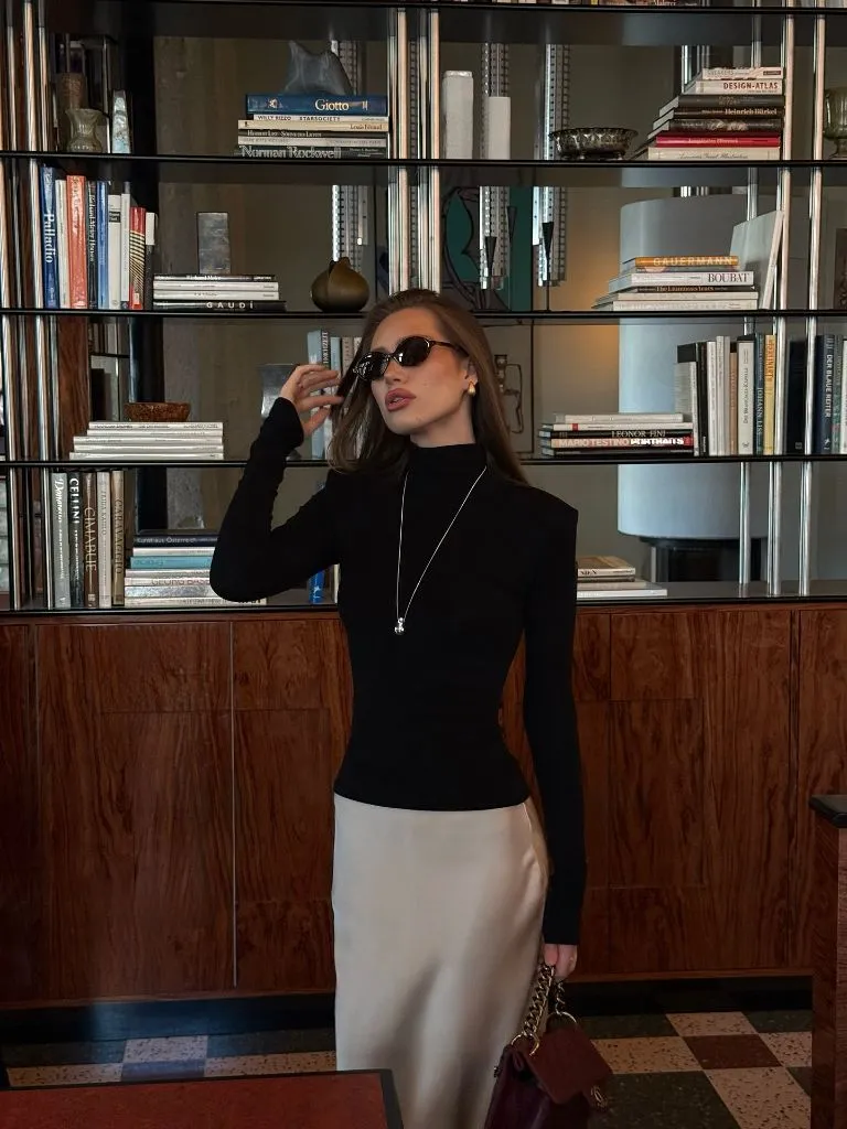 Front-facing black turtleneck and champagne satin skirt in hotel library