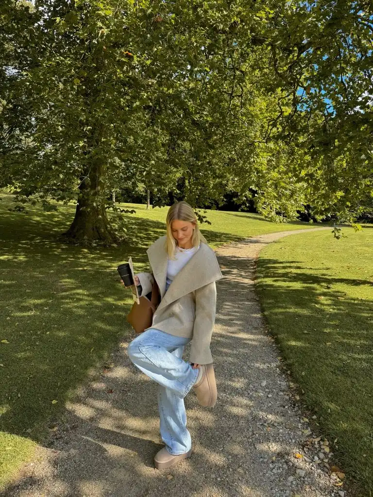 Oatmeal oversized wrap coat with light wash jeans and platform boots on a park path