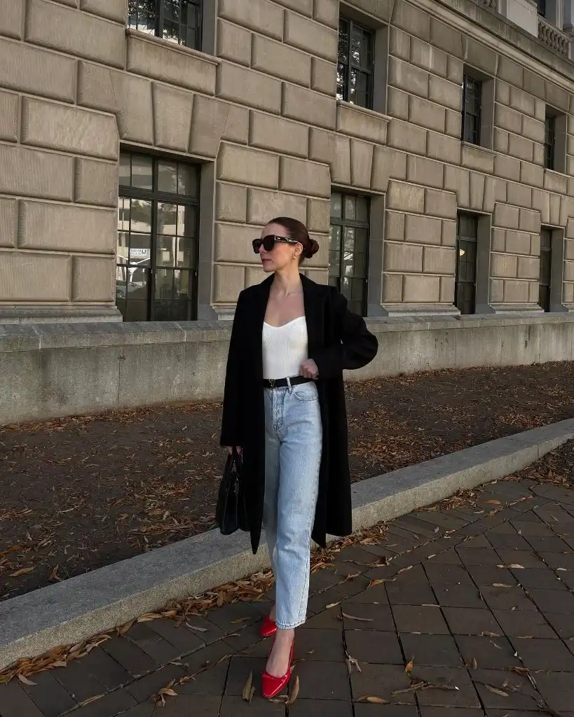 Black long coat with white ribbed tank, light-wash jeans, and red ballet flats