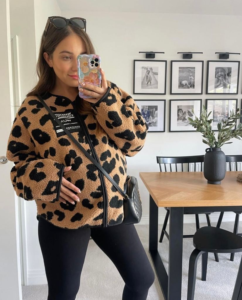 Mirror selfie of pregnant woman in leopard sherpa jacket, black leggings, and crossbody bag