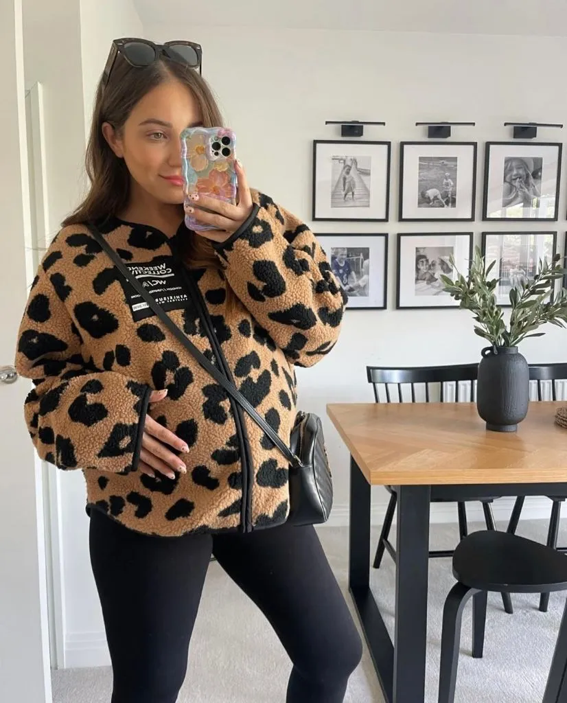 Mirror selfie of pregnant woman in leopard sherpa jacket, black leggings, and crossbody bag