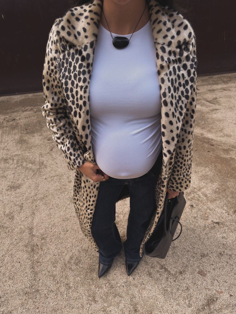 Close-up of pregnant woman in cheetah print coat, white tee, dark jeans, and black pointed boots