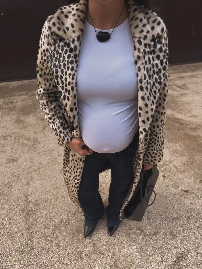 Close-up of pregnant woman in cheetah print coat, white tee, dark jeans, and black pointed boots