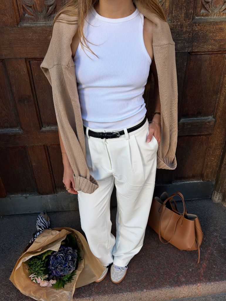 White ribbed tank top with beige cardigan, cream wide-leg trousers, black belt, and tan leather tote