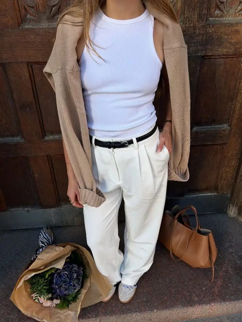 White ribbed tank top with beige cardigan, cream wide-leg trousers, black belt, and tan leather tote