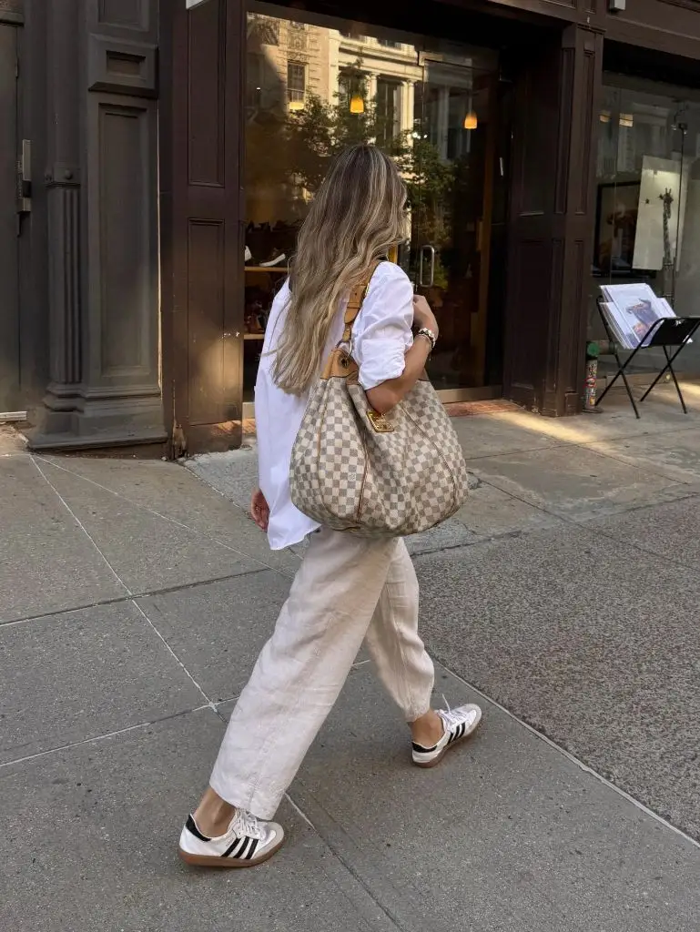 Back view walking in white oversized shirt, linen pants, and Adidas with LV bag