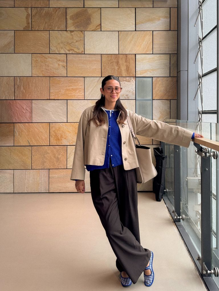 Beige boxy jacket over cobalt blue knit cardigan with dark wide-leg trousers and gingham shoes