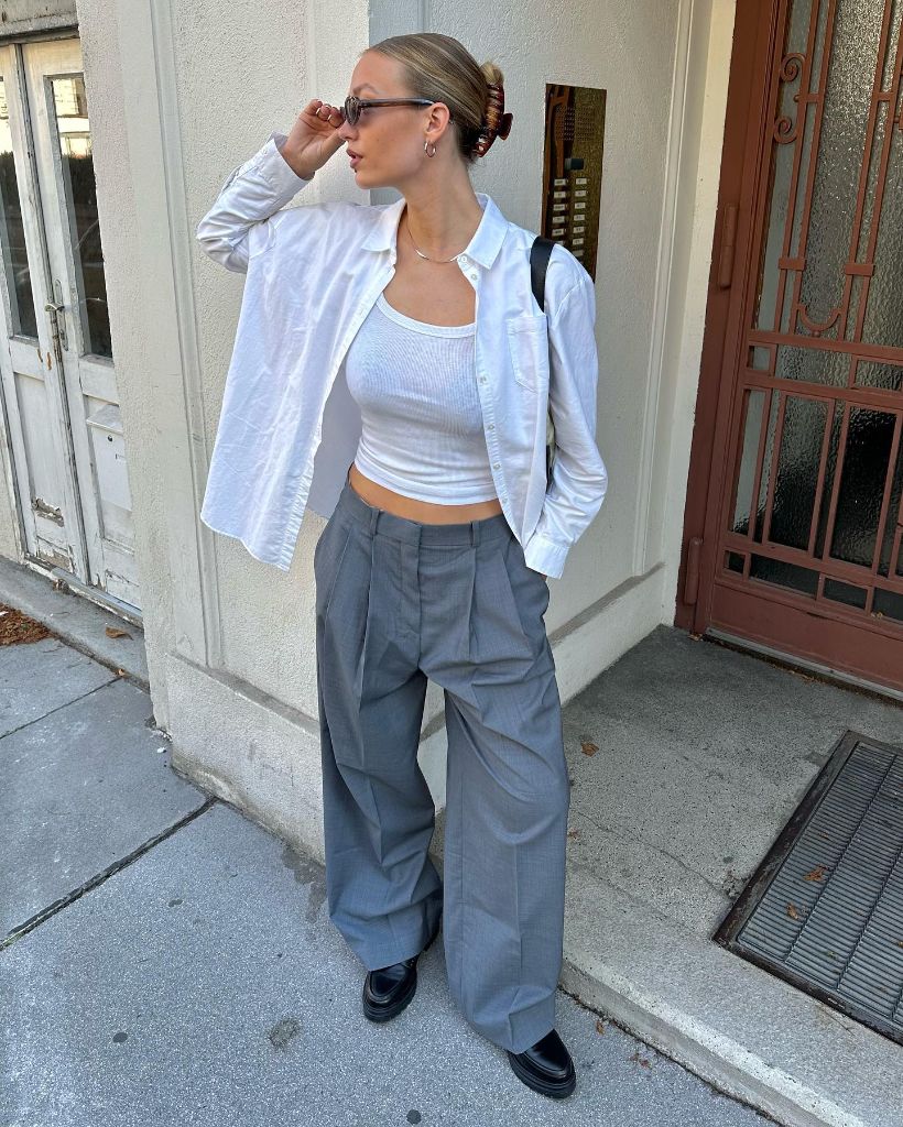White oversized button-down shirt over white tank top with grey wide-leg pleated trousers and black loafers