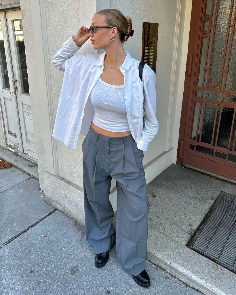 White oversized button-down shirt over white tank top with grey wide-leg pleated trousers and black loafers