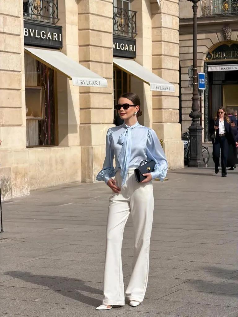 Light blue satin blouse with white trousers in front of Bulgari
