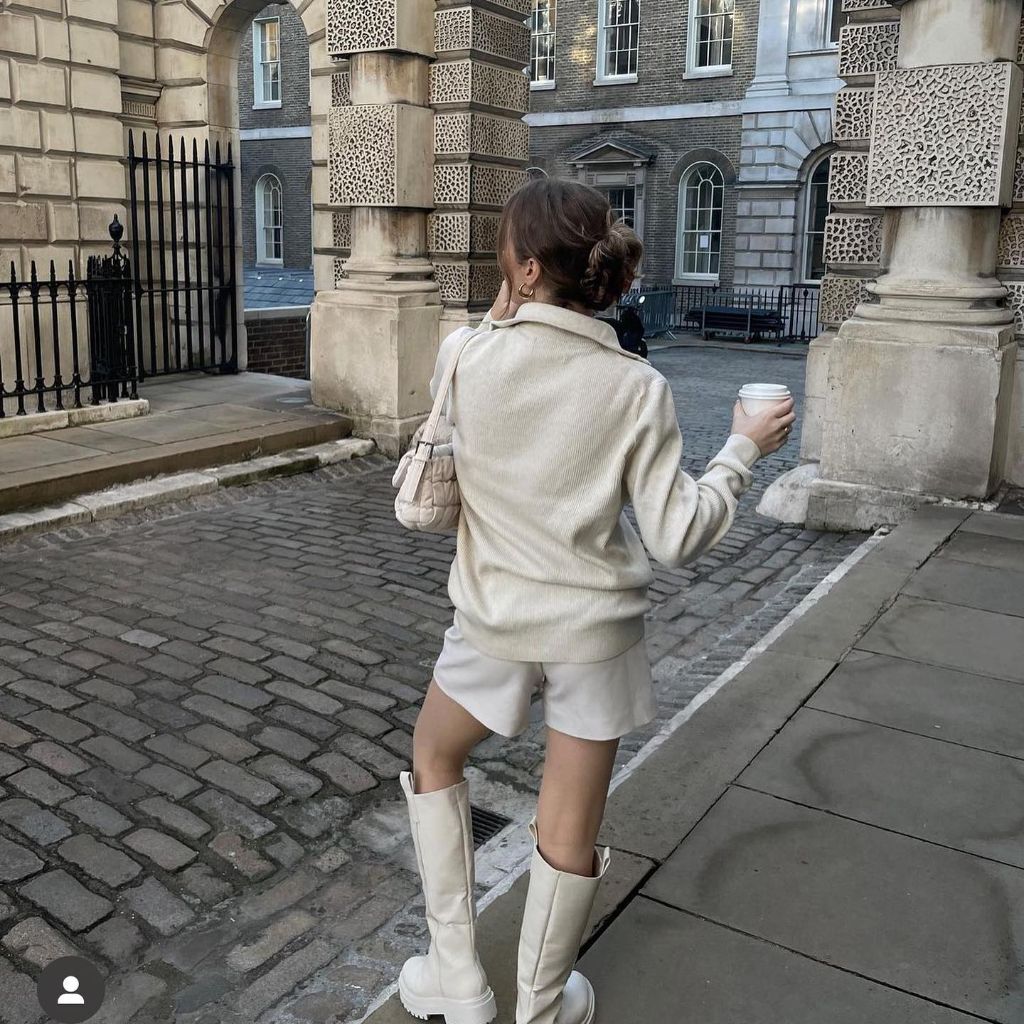 All-cream outfit with knit polo sweater, matching shorts, knee-high boots, and quilted cream bag in London courtyard