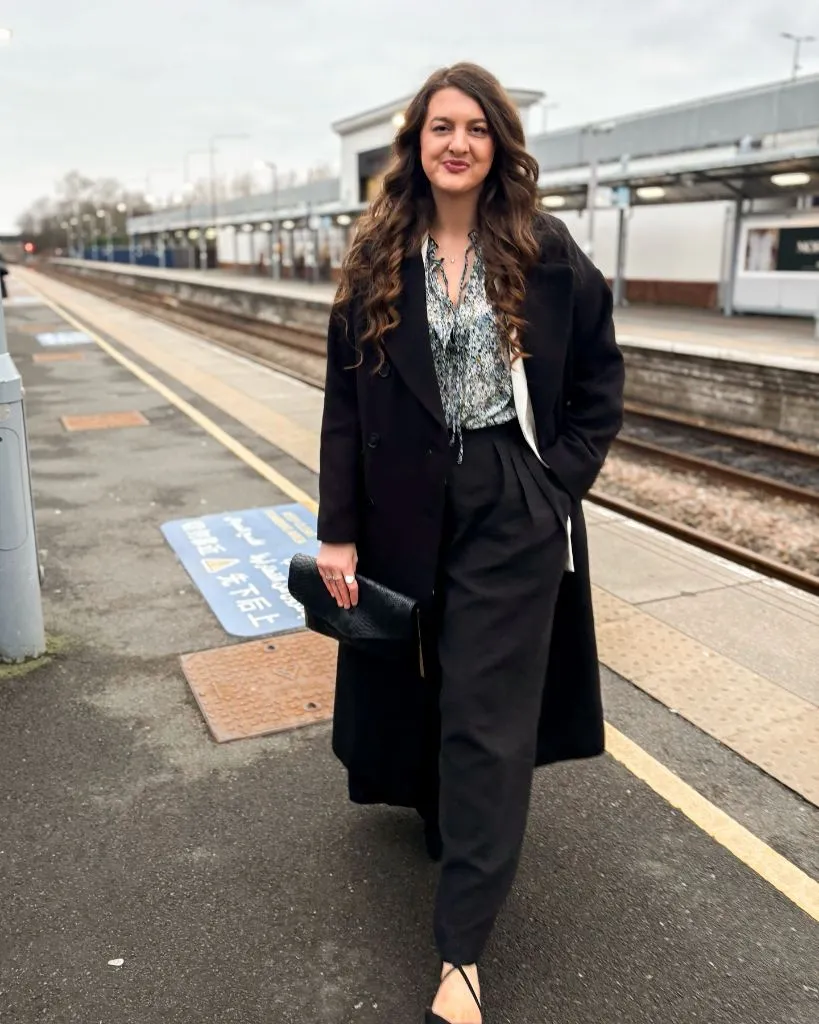 Black overcoat with printed blouse and wide-leg trousers at train platform
