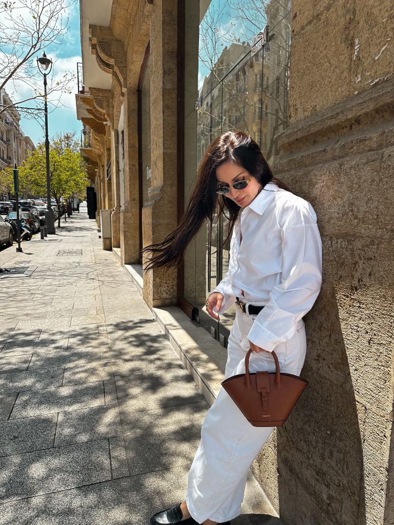 All-white outfit with oversized shirt and tan structured leather bag