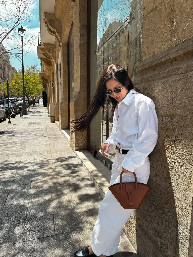 All-white outfit with oversized shirt and tan structured leather bag