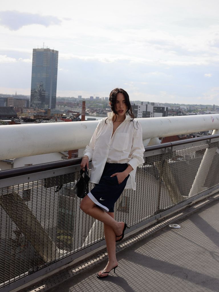 White button-down shirt with Nike shorts and heeled sandals on a bridge