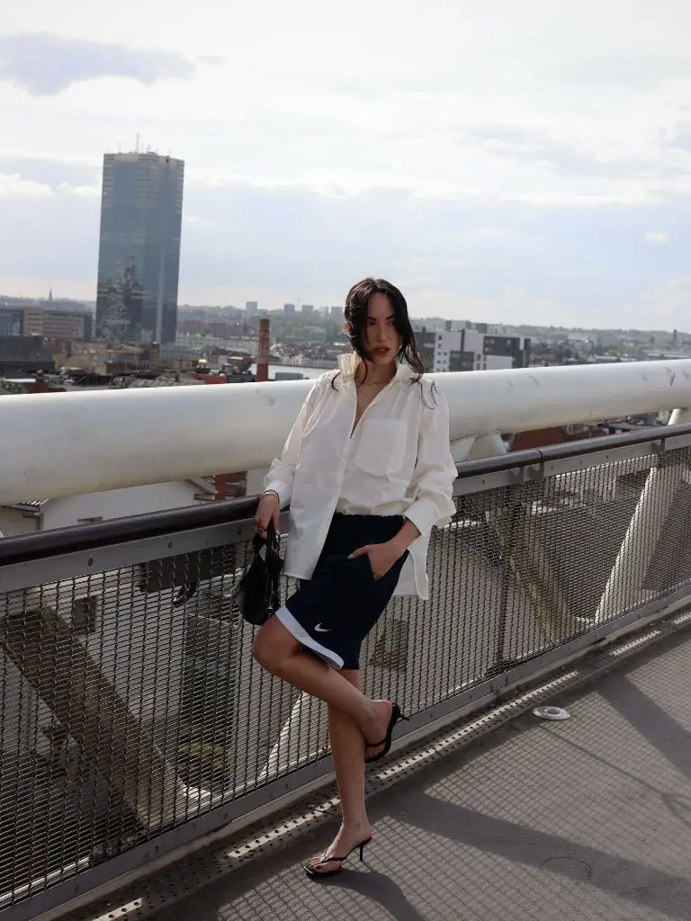 White button-down shirt with Nike shorts and heeled sandals on a bridge