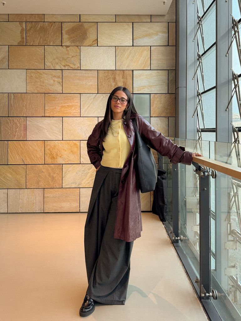 Burgundy leather coat over yellow sweater with dark wide-leg trousers