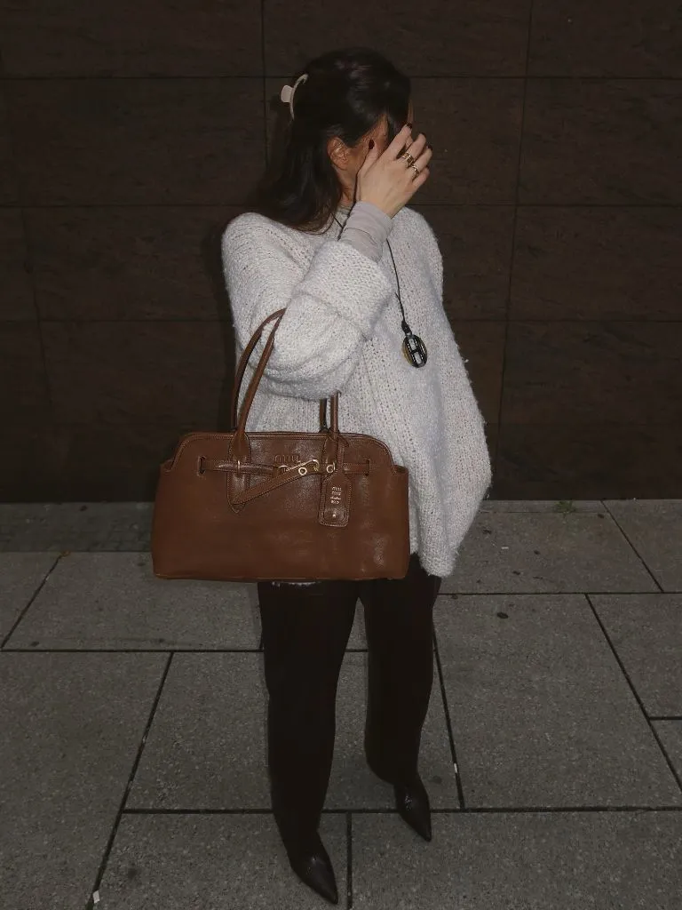 Person in oversized cream knit sweater, dark trousers, pointed boots, and tan Miu Miu bag