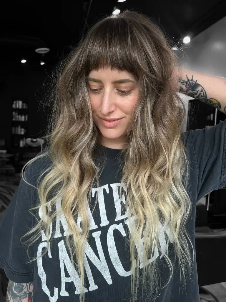 Brunette root melting into blonde ends with a blunt fringe and beachy waves