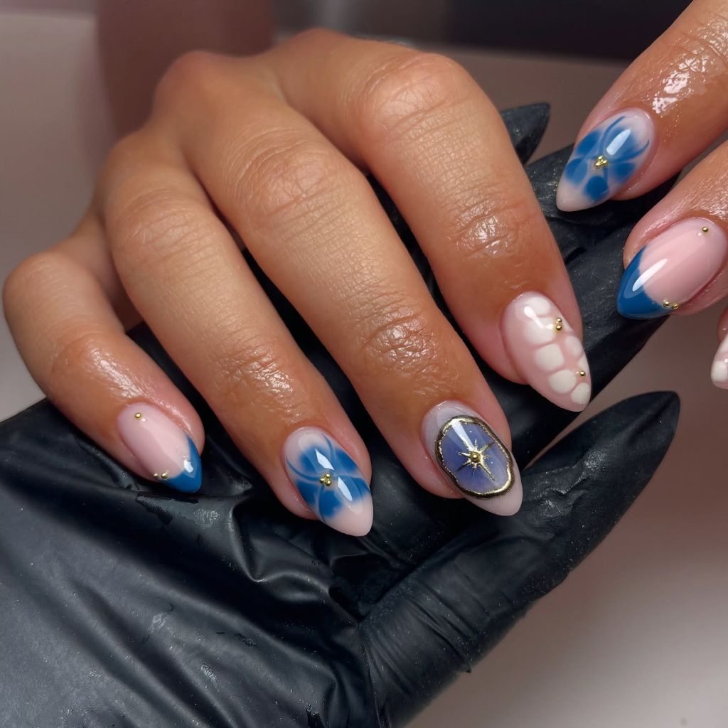 Blue floral and celestial nail art with gold star accents on almond nails August nails color 2026 ideas
