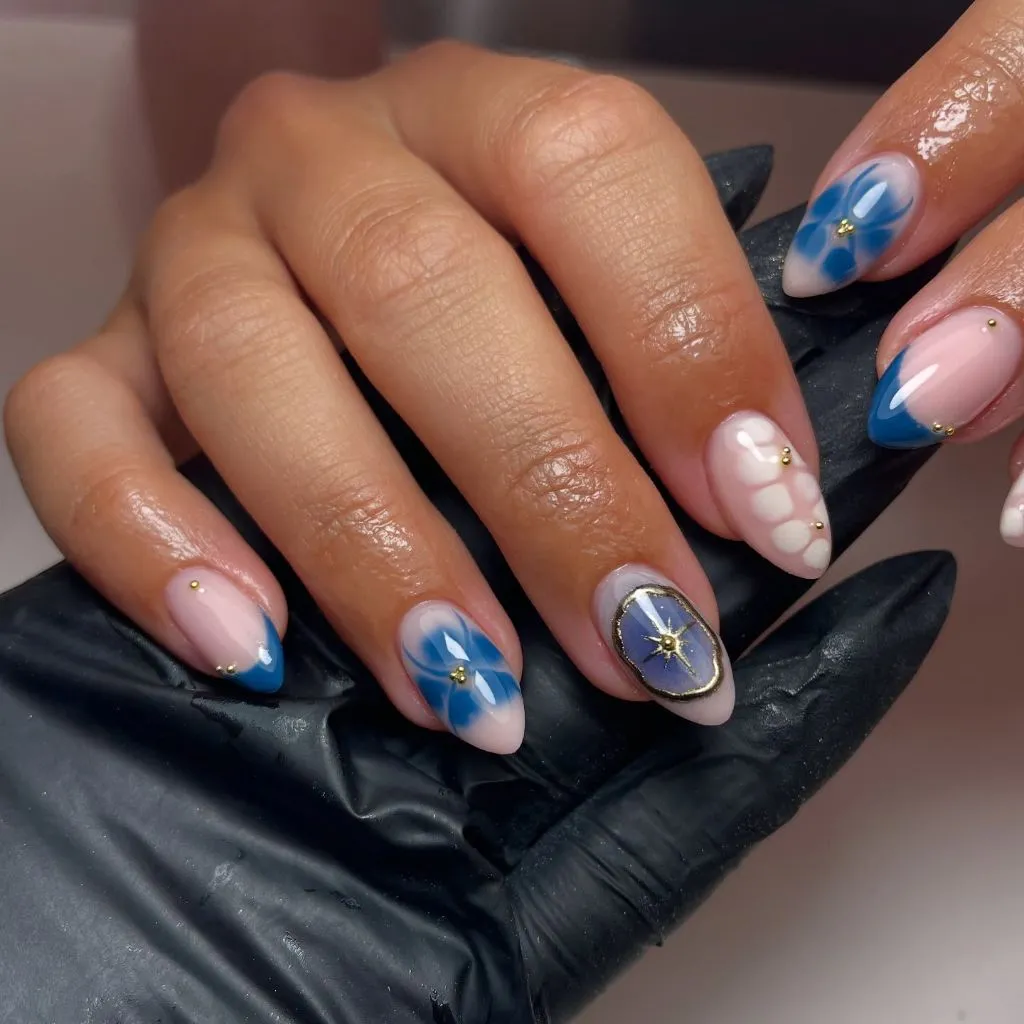 Blue floral and celestial nail art with gold star accents on almond nails August nails color 2026 ideas