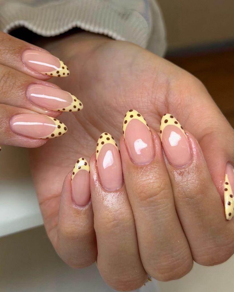 Butter yellow French tips with brown polka dots on almond nails August nails color 2026 ideas