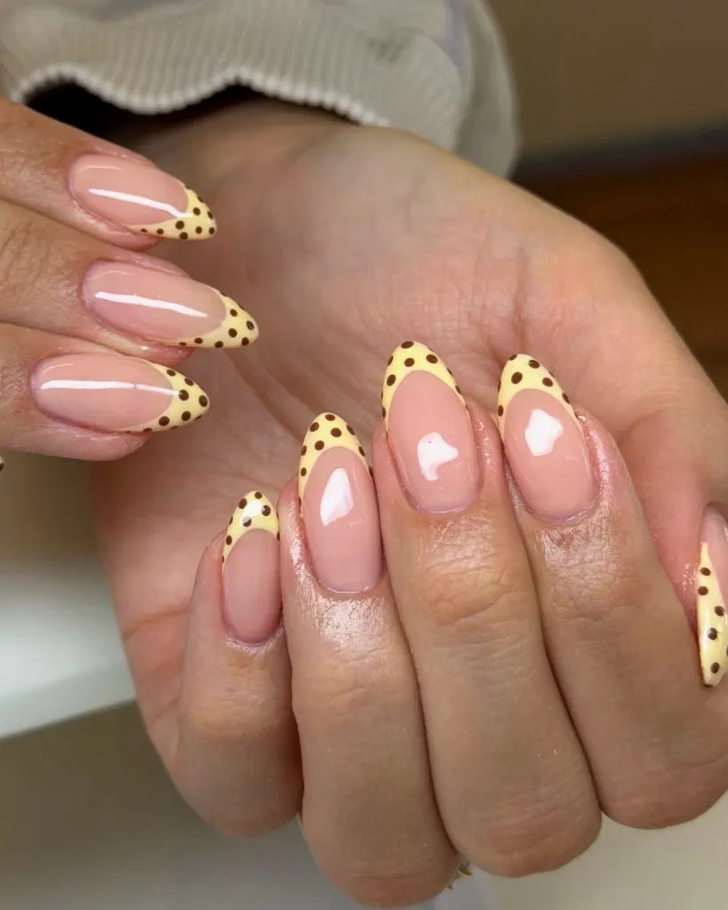 Butter yellow French tips with brown polka dots on almond nails August nails color 2026 ideas