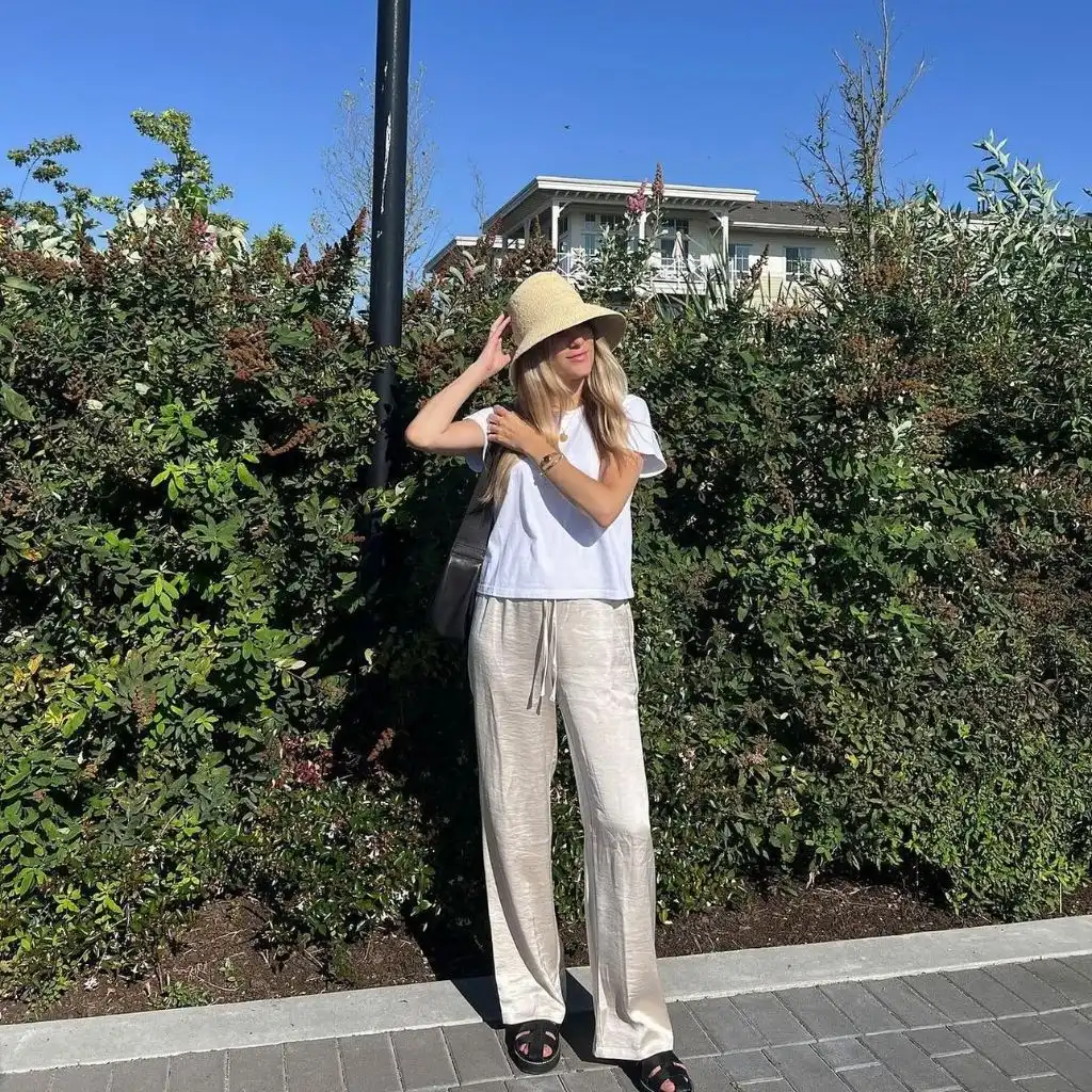White tee with beige linen pants, straw hat, and black sandals
