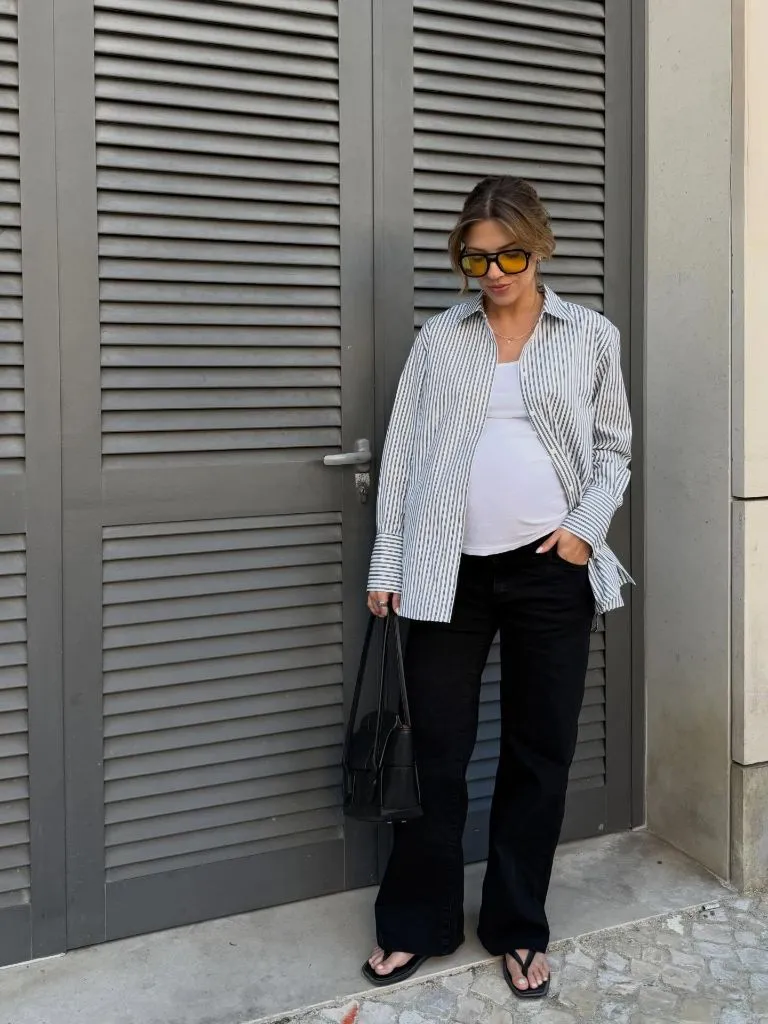 Pregnant woman in striped button-down shirt, black wide-leg pants, flip-flop sandals, and black bag