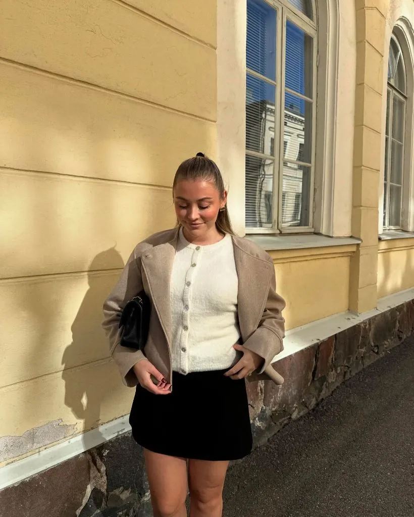 Taupe wool bomber jacket over white button-front cardigan and black mini skirt with black bag