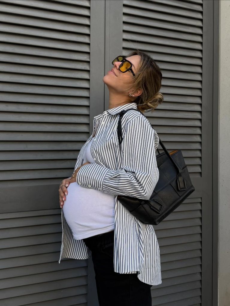Side profile of pregnant woman in striped shirt, white tee, and black bag looking upward