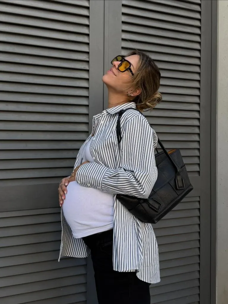 Side profile of pregnant woman in striped shirt, white tee, and black bag looking upward