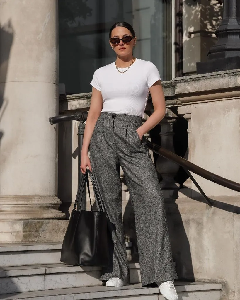 White fitted tee with grey wide-leg trousers, sneakers, and black tote