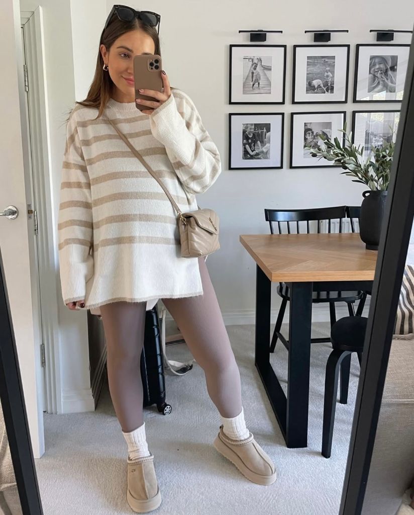 Mirror selfie of pregnant woman in cream and tan striped oversized sweater, mauve leggings, and platform UGGs