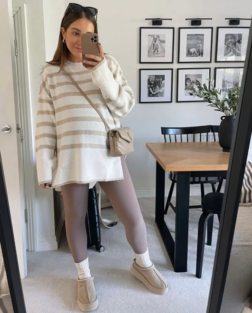 Mirror selfie of pregnant woman in cream and tan striped oversized sweater, mauve leggings, and platform UGGs