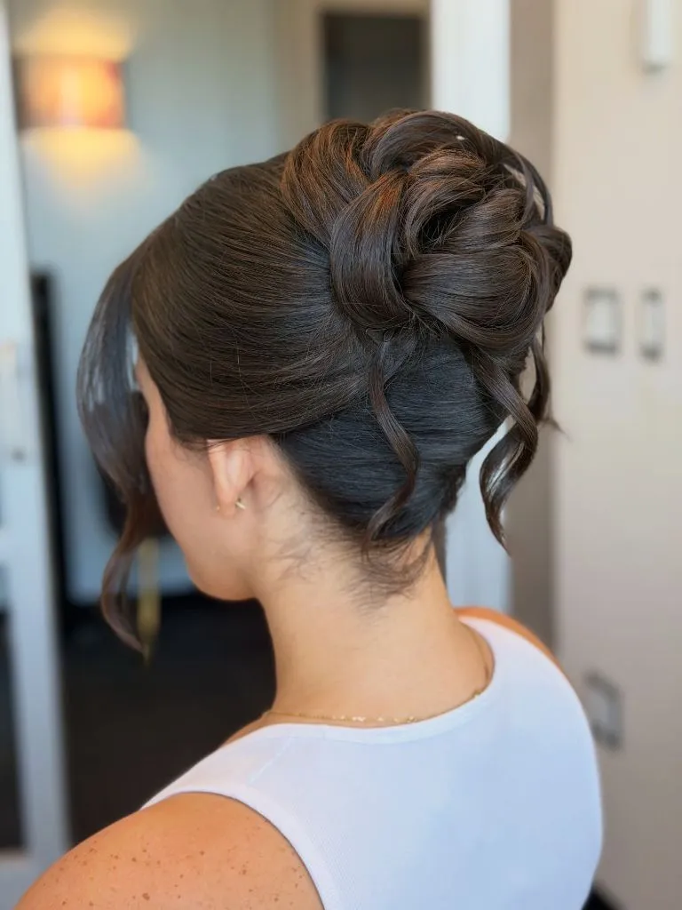 Fall Hairstyles for Wedding Guests 2026 Voluminous Curled High Bun with Wispy Pieces