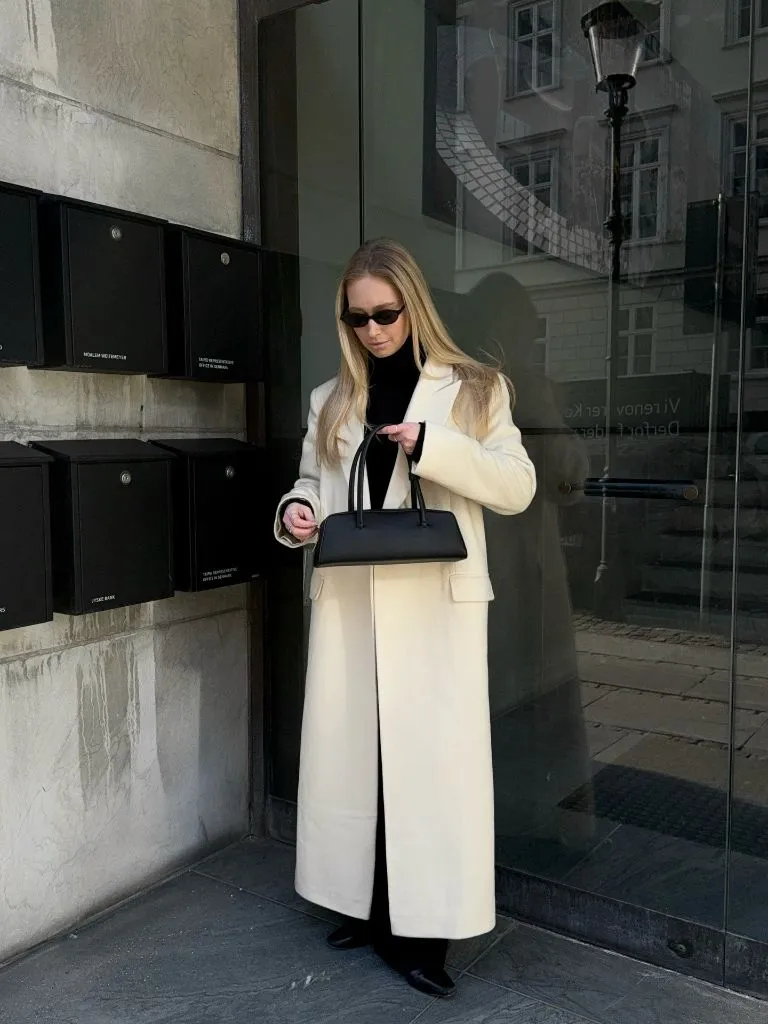 Ivory long coat with black turtleneck and structured bag